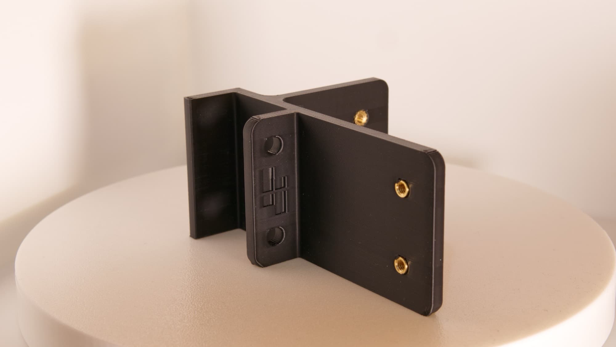 Close-up of a black 3D-printed mount, brass threaded inserts seated in three bosses